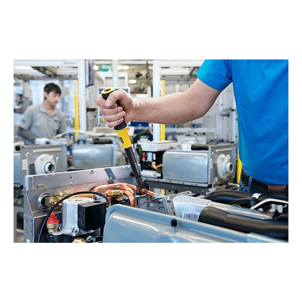 A person using a torque wrench on a mechanical assembly in a factory setting