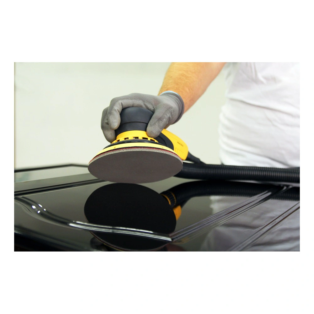 אדם מחזיק משייפת חשמלית על משטח שחור מבריק, כנראה בזמן שיוף או ליטוש