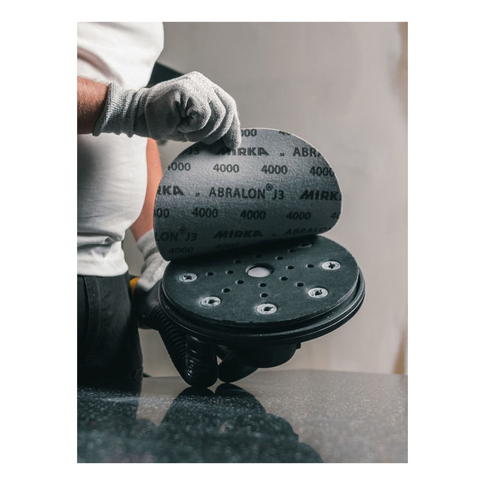 A gloved person holds a gray sanding disc above a perforated round sanding