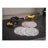 A yellow-and-black handheld sander rests on a dark table, with several round