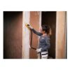 A woman uses a yellow and black hand sander with a suction hose, against