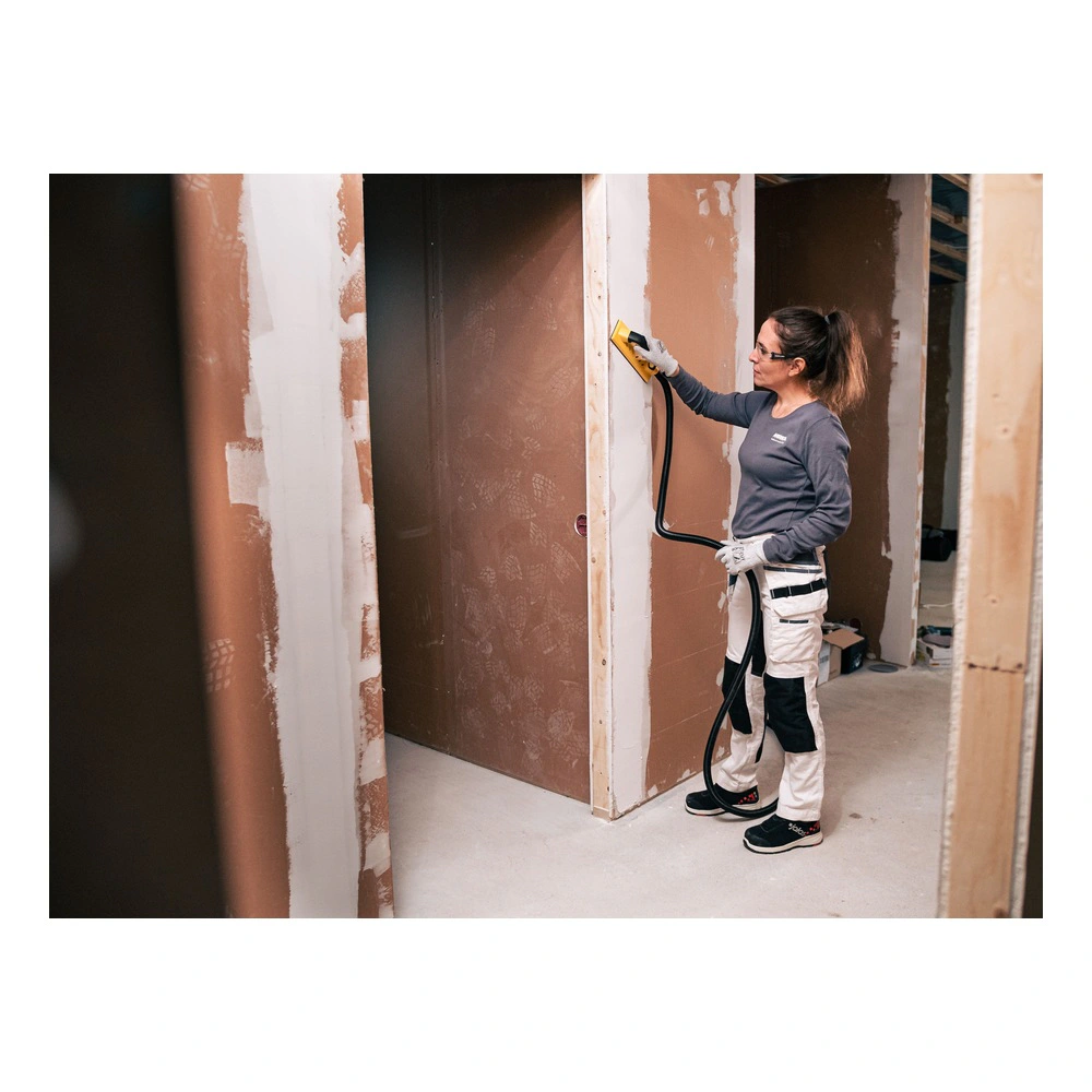 A person is using a mesh sander on an unfinished interior wall