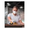 A woman wearing a protective mask uses a yellow-and-black power sander