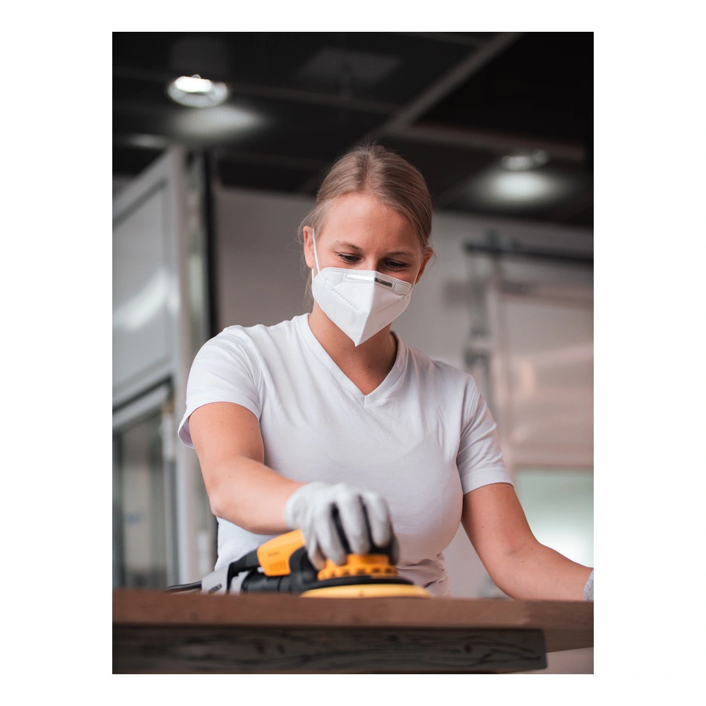 A woman wearing a protective mask uses a yellow-and-black power sander