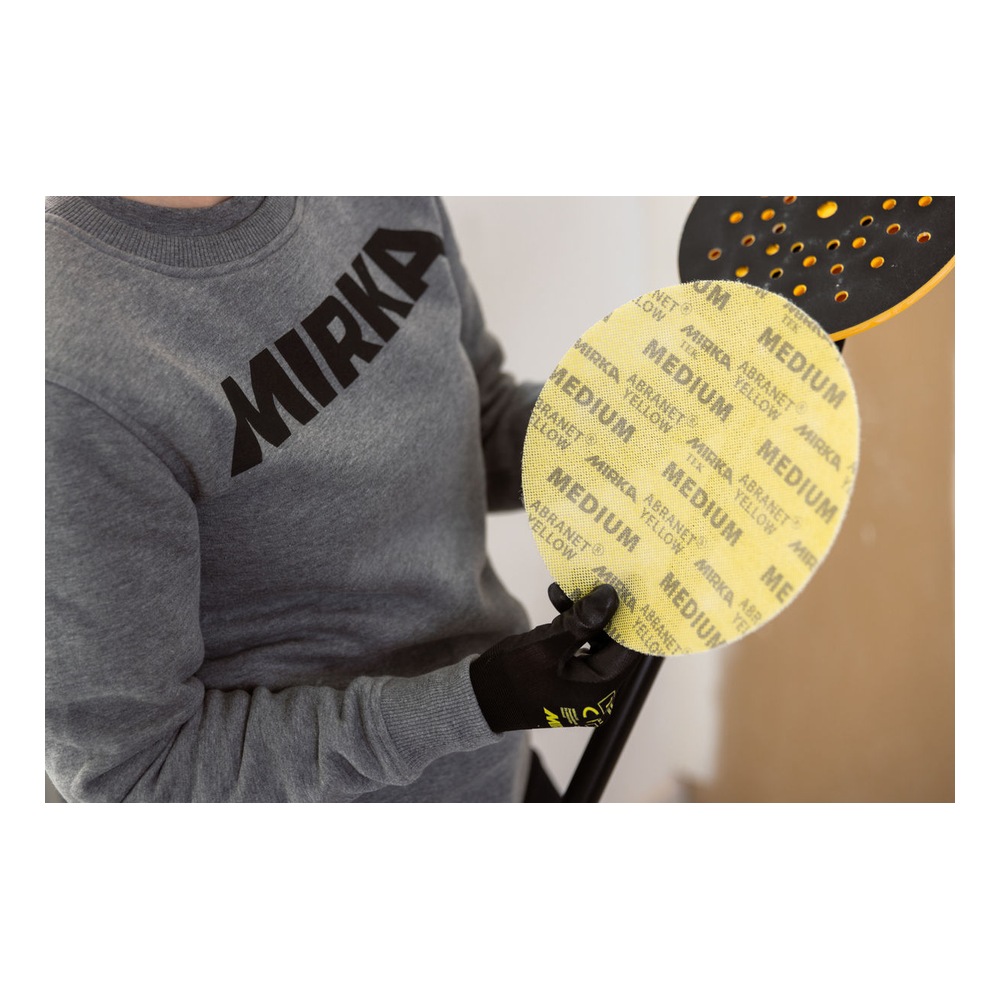A person is holding a yellow perforated sanding disc, with a partially