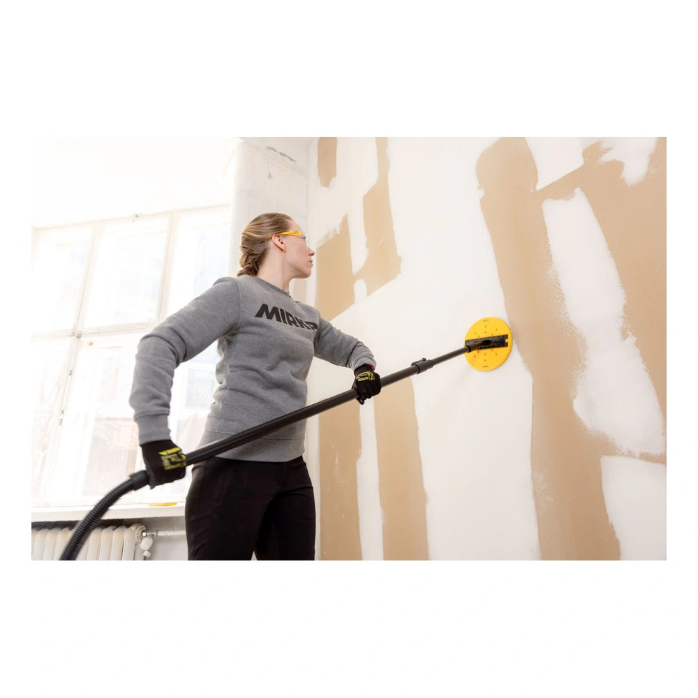 A person is using a long sanding pole with a yellow disc on a drywall