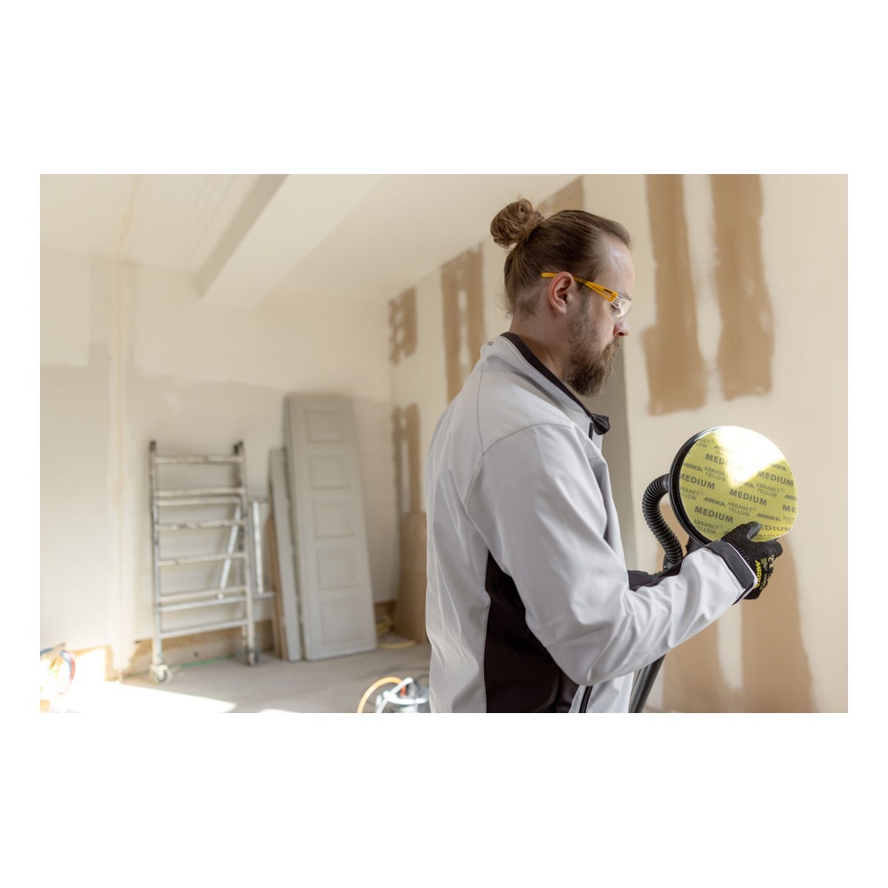 A person standing in a renovation room holding a round sander attached