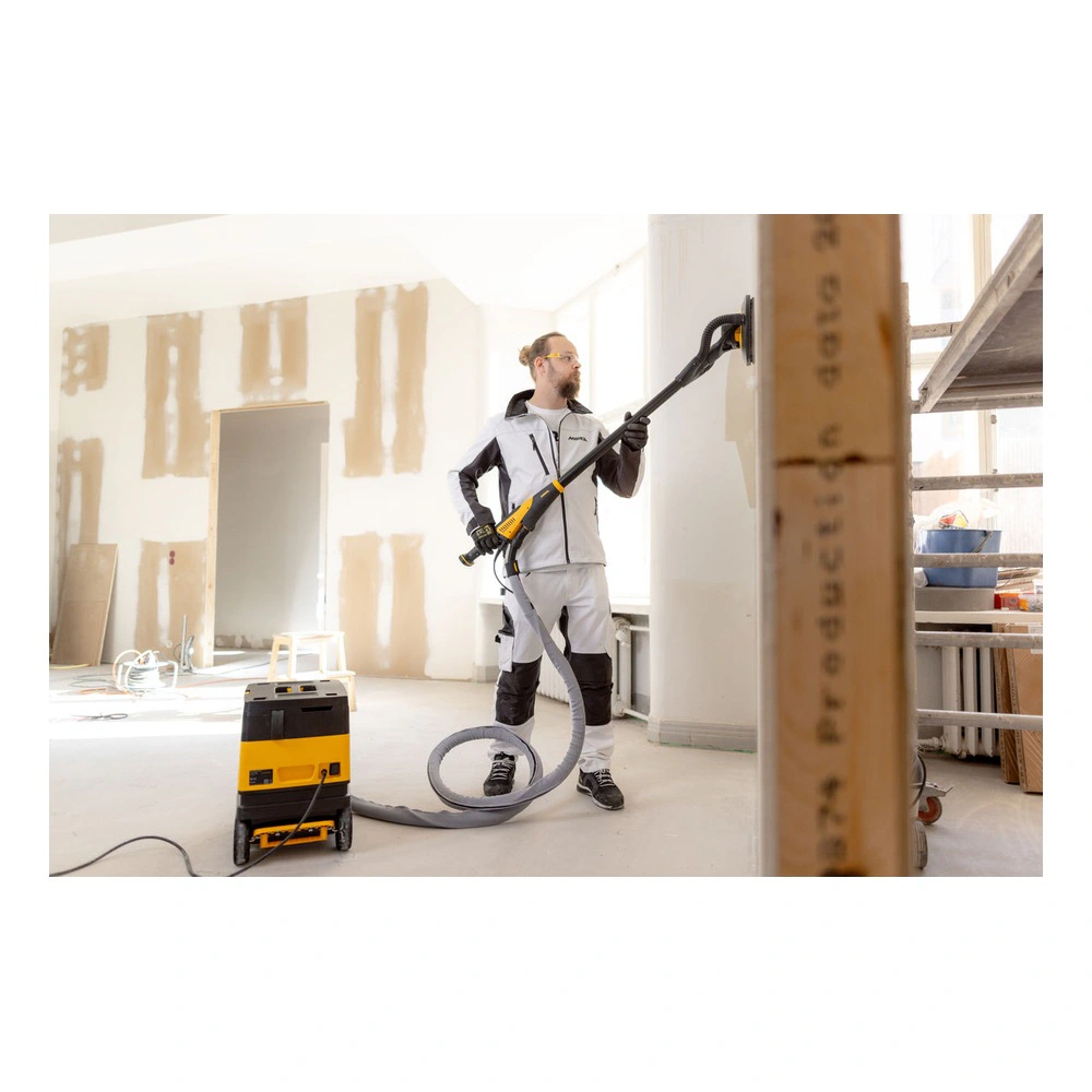 A person uses a long wall sander connected to a vacuum, inside a renovation