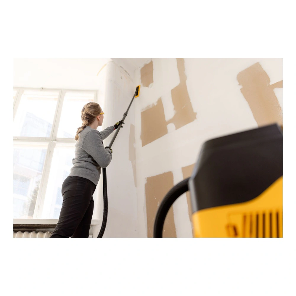 A person sands a high wall with a long sander near a window, with a blurred