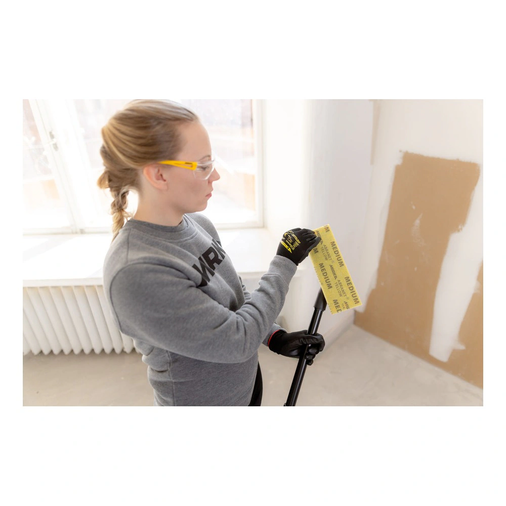 A person in a workroom holding a yellow sanding sheet and working