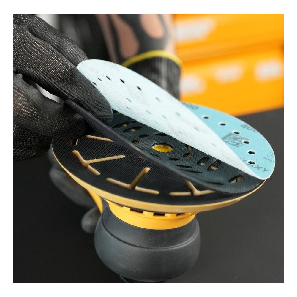 A gloved hand holds a round sanding pad with several layered perforated