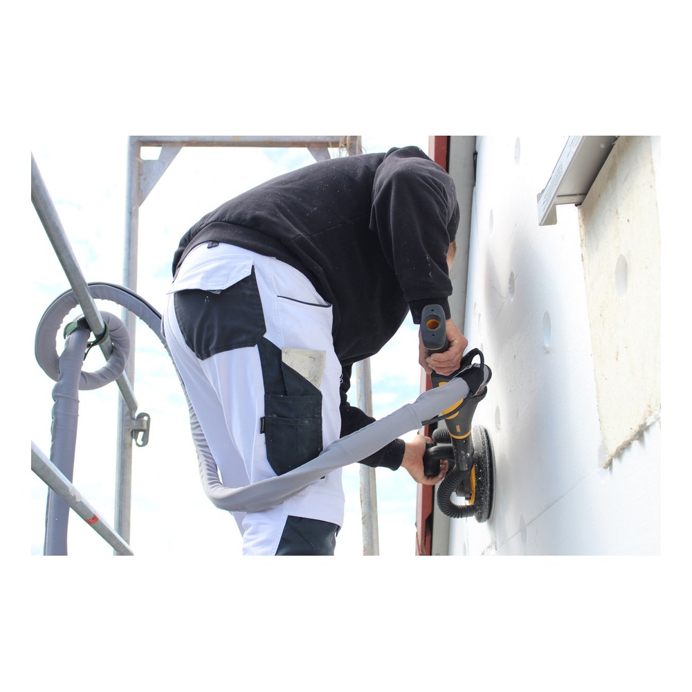 A person is using a hand sander against a white wall at a work site