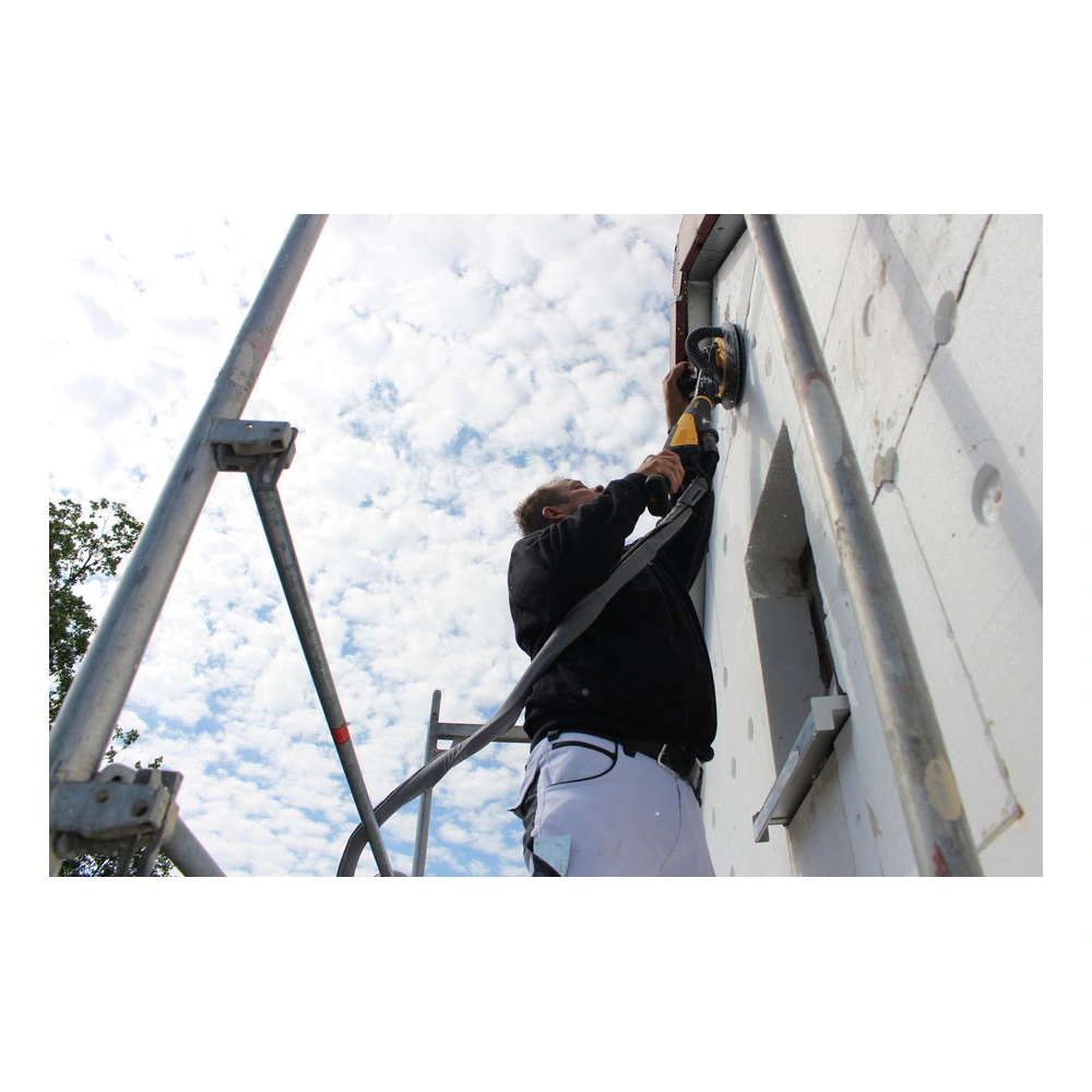 A person stands on scaffolding sanding an exterior white wall with a round