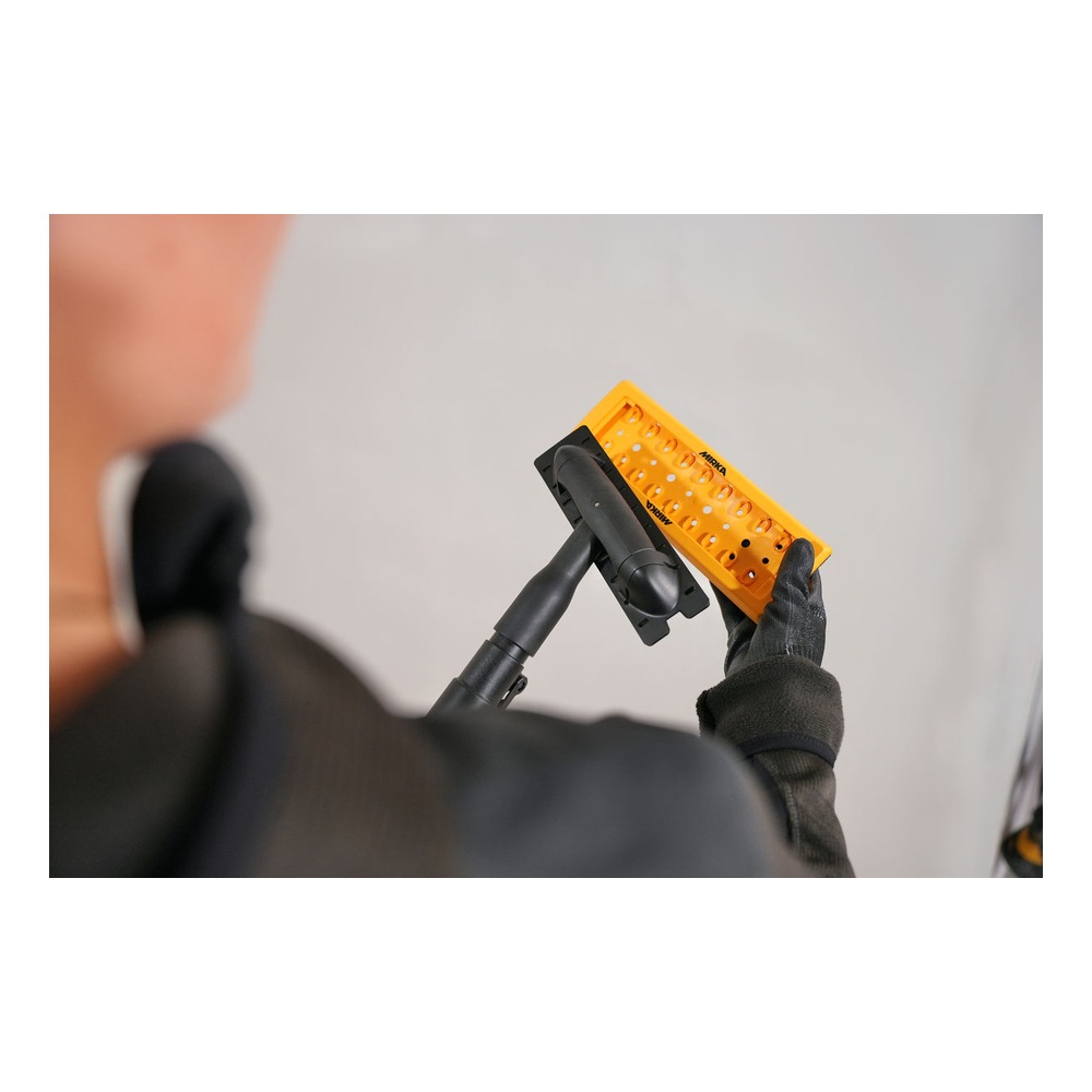 A person holds a telescopic hand sander against a light wall; only the back