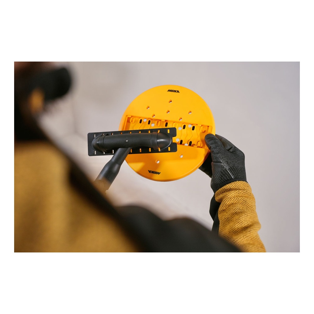 A person is holding a round yellow sanding head with suction holes, attached