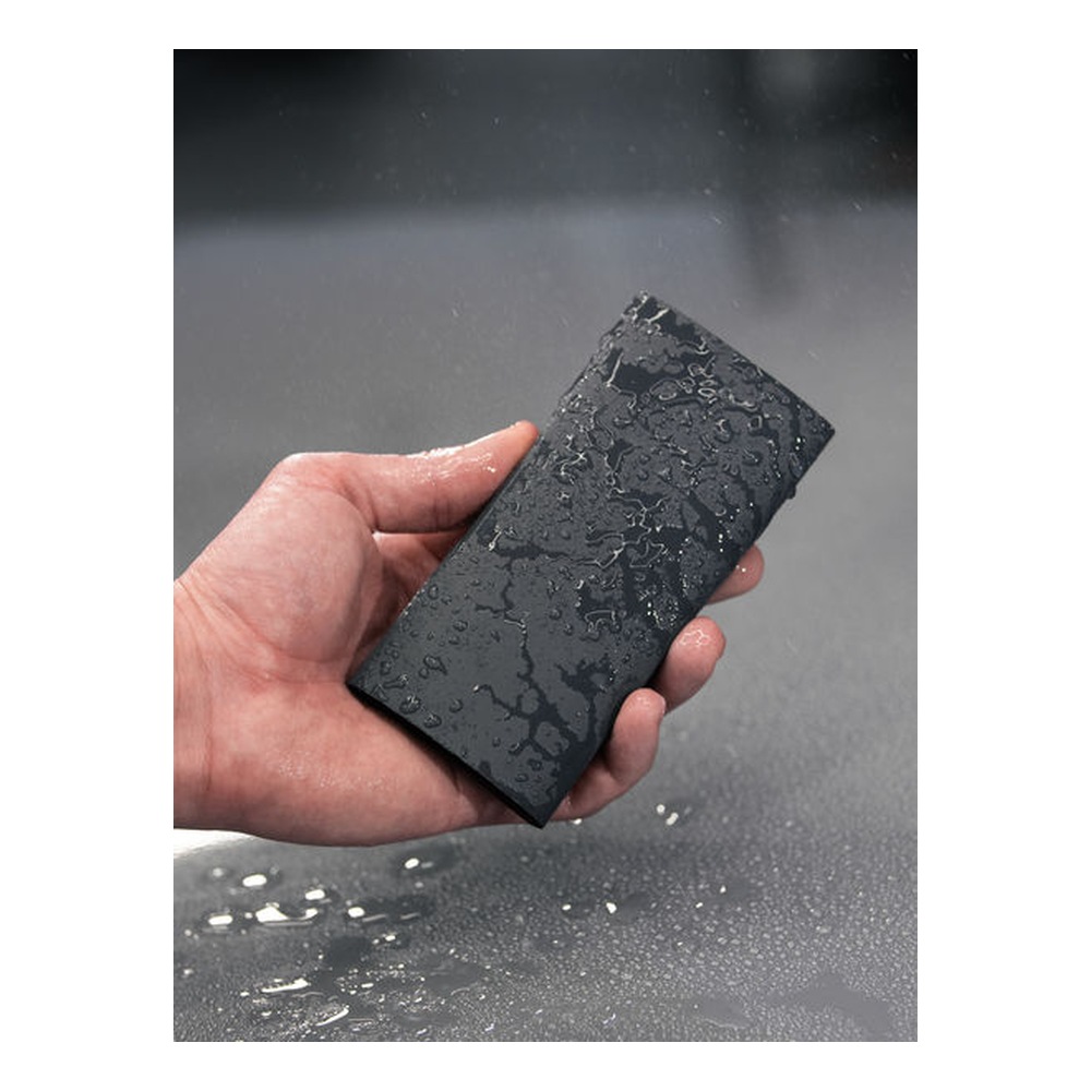 A hand holding a wet black sheet of sanding paper above a wet surface