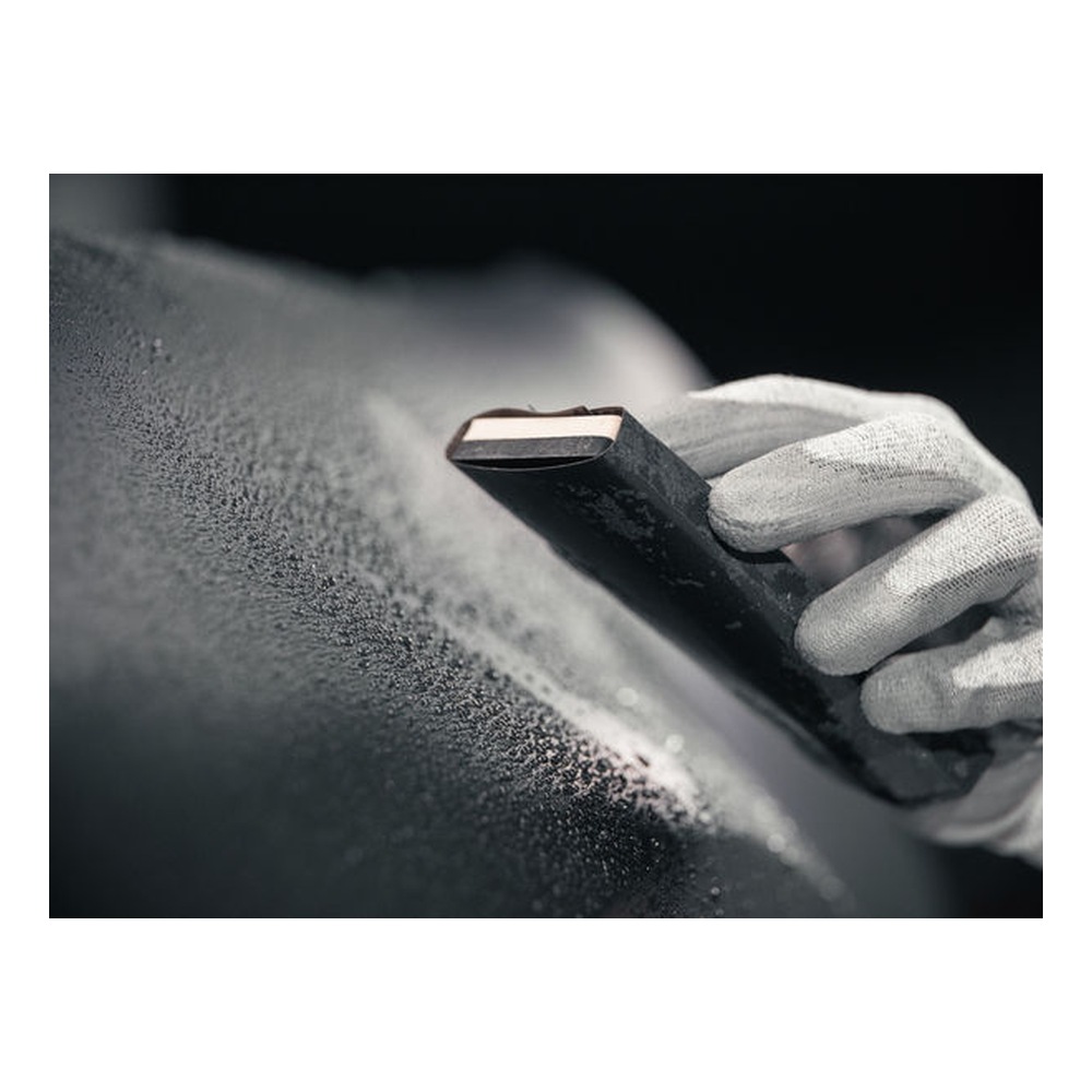 Close-up of a gloved hand holding sanding paper against a black surface