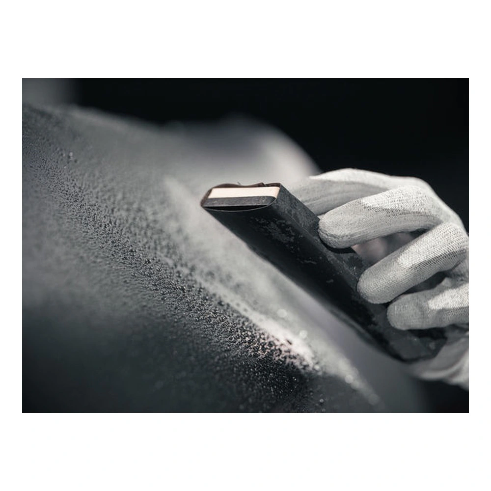 Close-up of a gloved hand holding sanding paper against a black surface