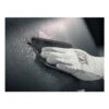 A gloved hand holding a piece of sanding paper against a black surface