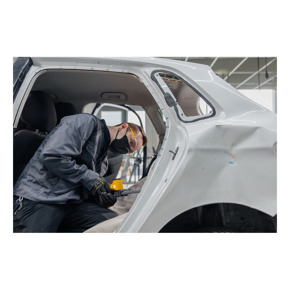 A person working inside a white vehicle body, using a small yellow and black