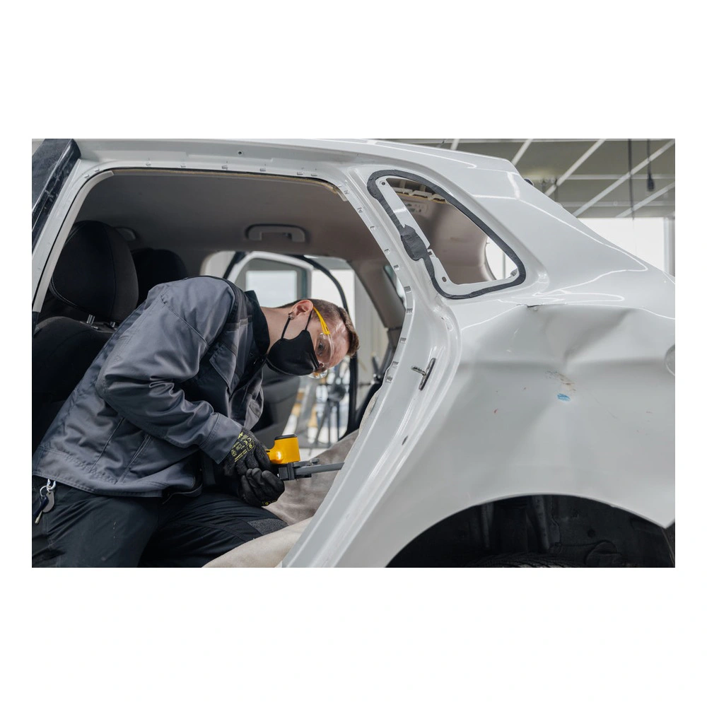 A person working inside a white vehicle body, using a small yellow and black