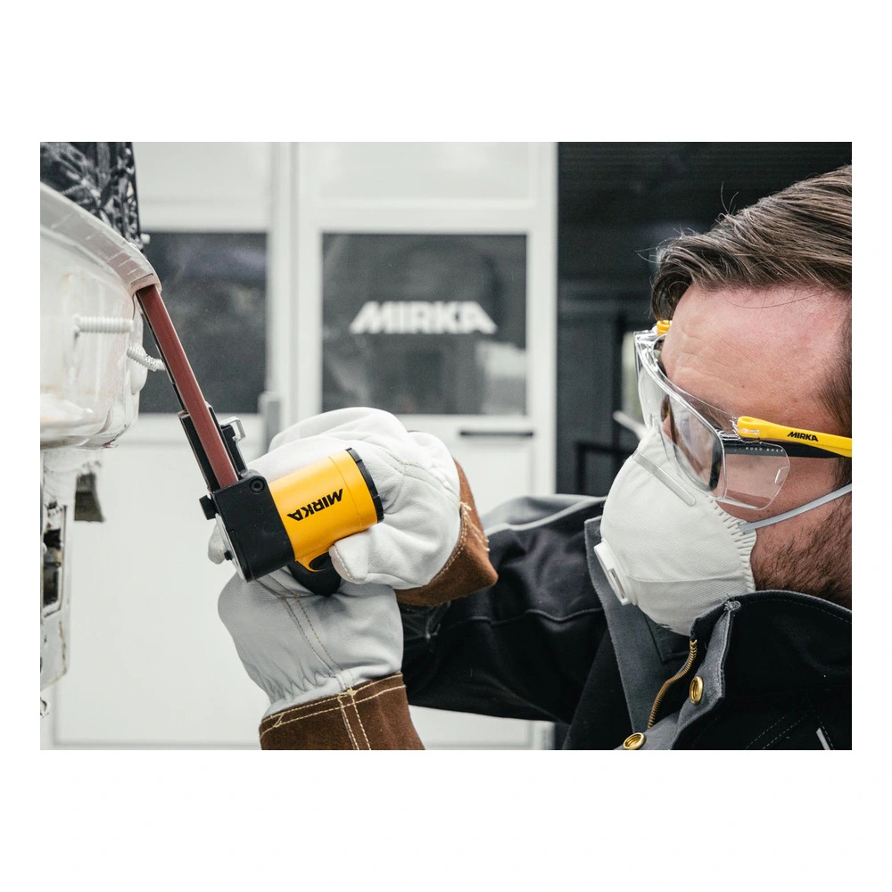 A person wearing safety glasses and a dust mask operates a small belt