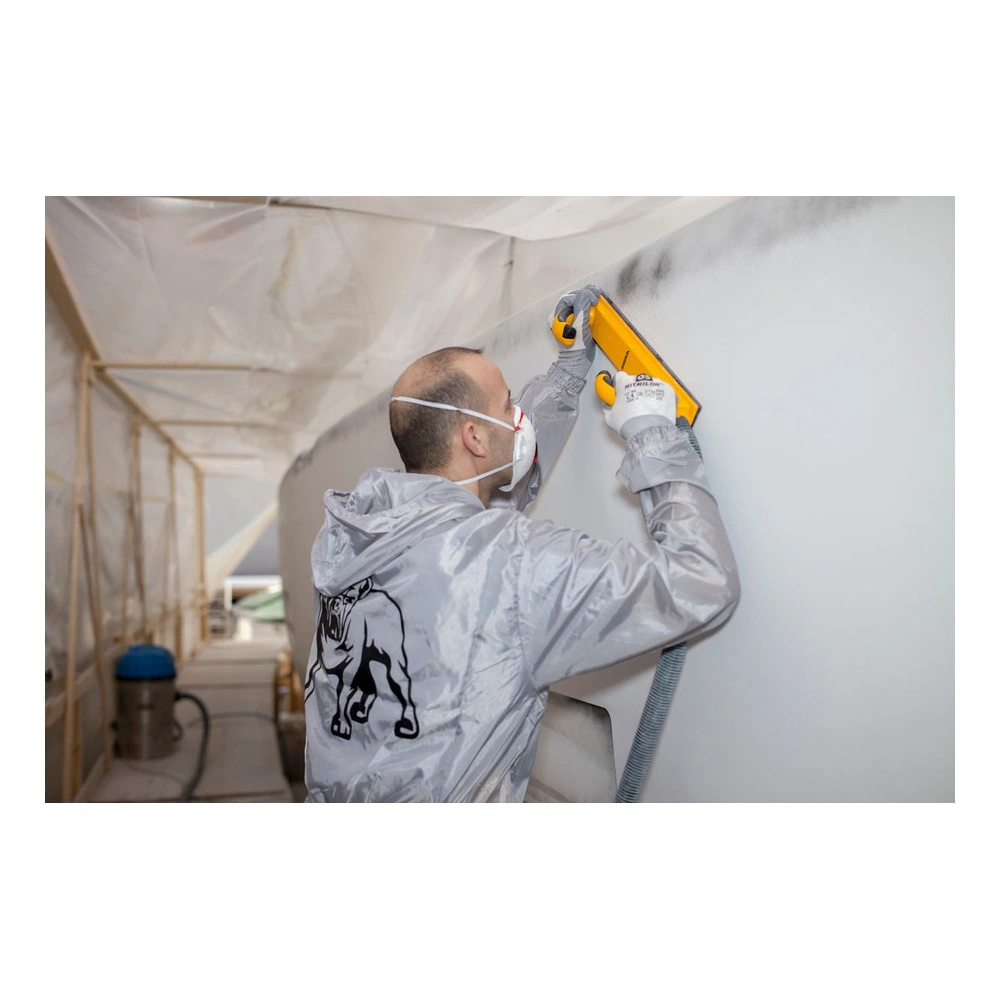 A person wearing a protective mask uses a yellow sanding board on a large