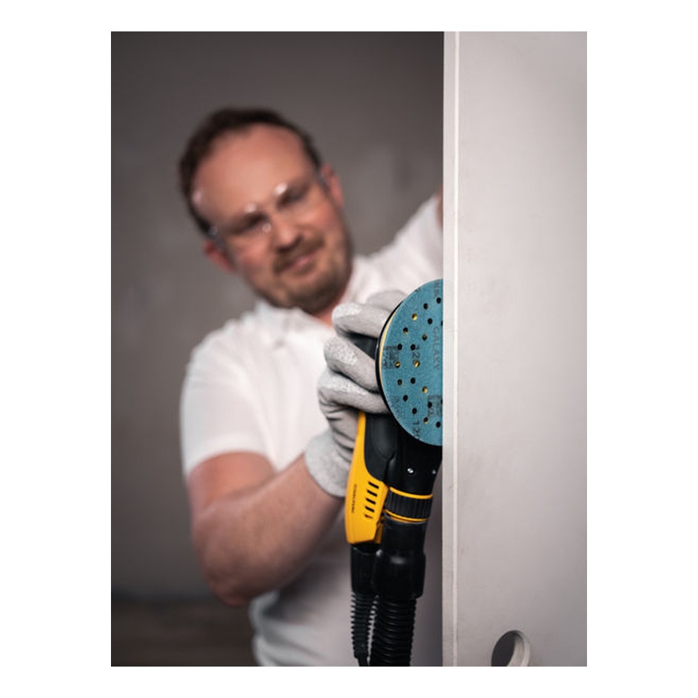 A person is using a round sander with a blue disc near the edge