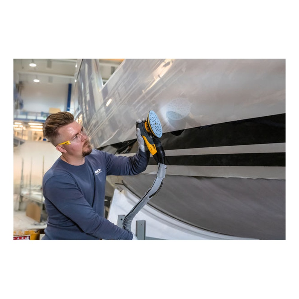 A person is using a hand sander on a large light-colored surface