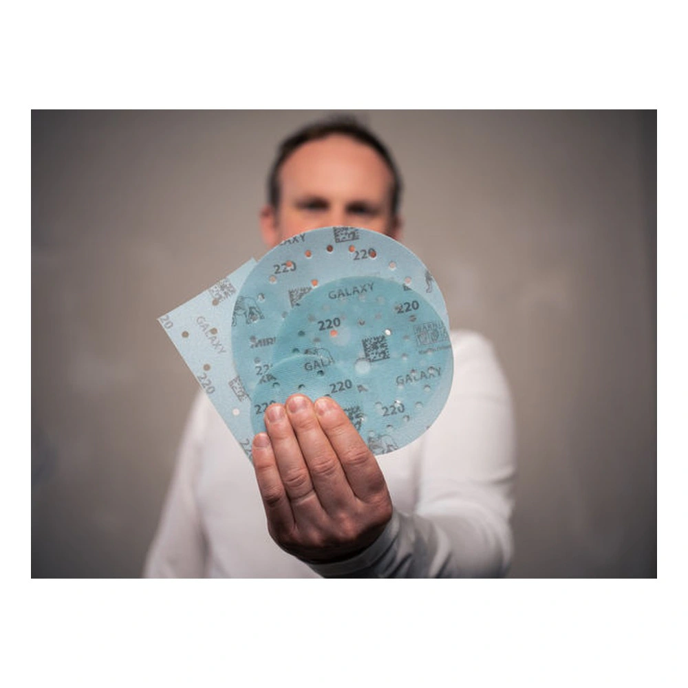 A person is holding three blue sanding discs with holes and printed text