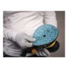 Gloved hands hold a round hand sander with a blue sanding pad