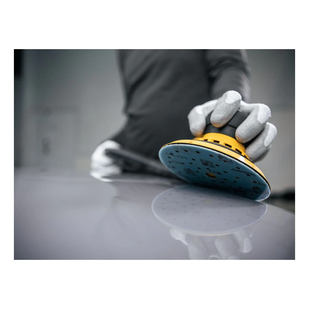 A gloved hand holds a round sander on a glossy surface, with a blue-gray