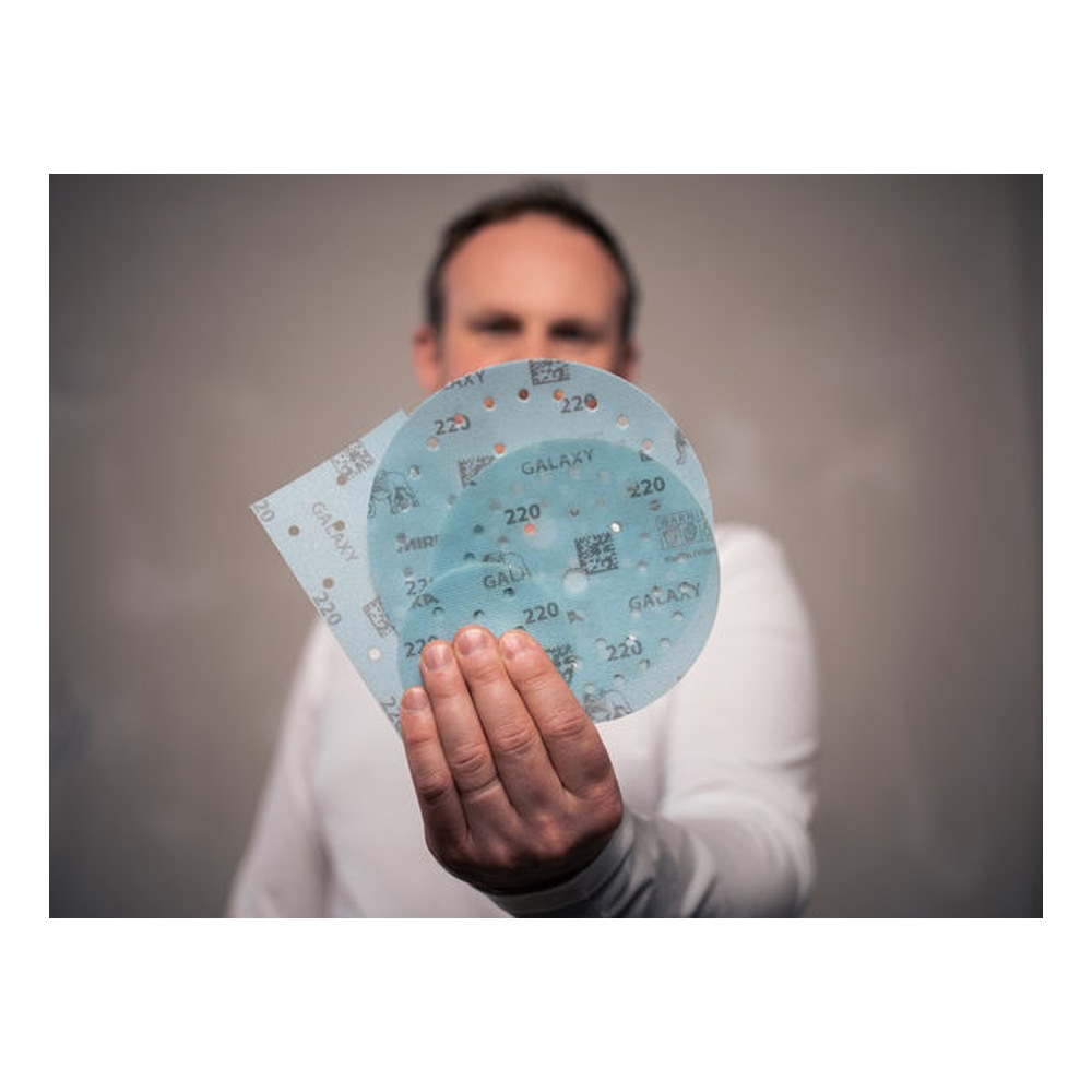 A person is holding several round light-blue sanding discs toward the camera