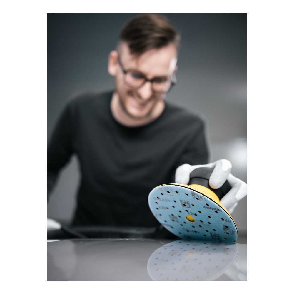 A person wearing gloves holding a sanding tool with a blue-gray perforated
