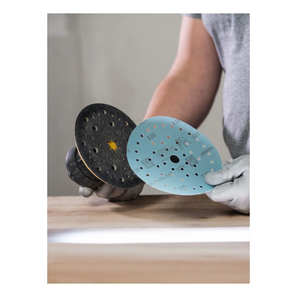 A person holds two perforated round sanding discs above a wooden surface