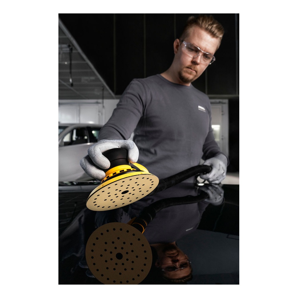 A man wearing gloves and safety glasses uses a round sander on a shiny car
