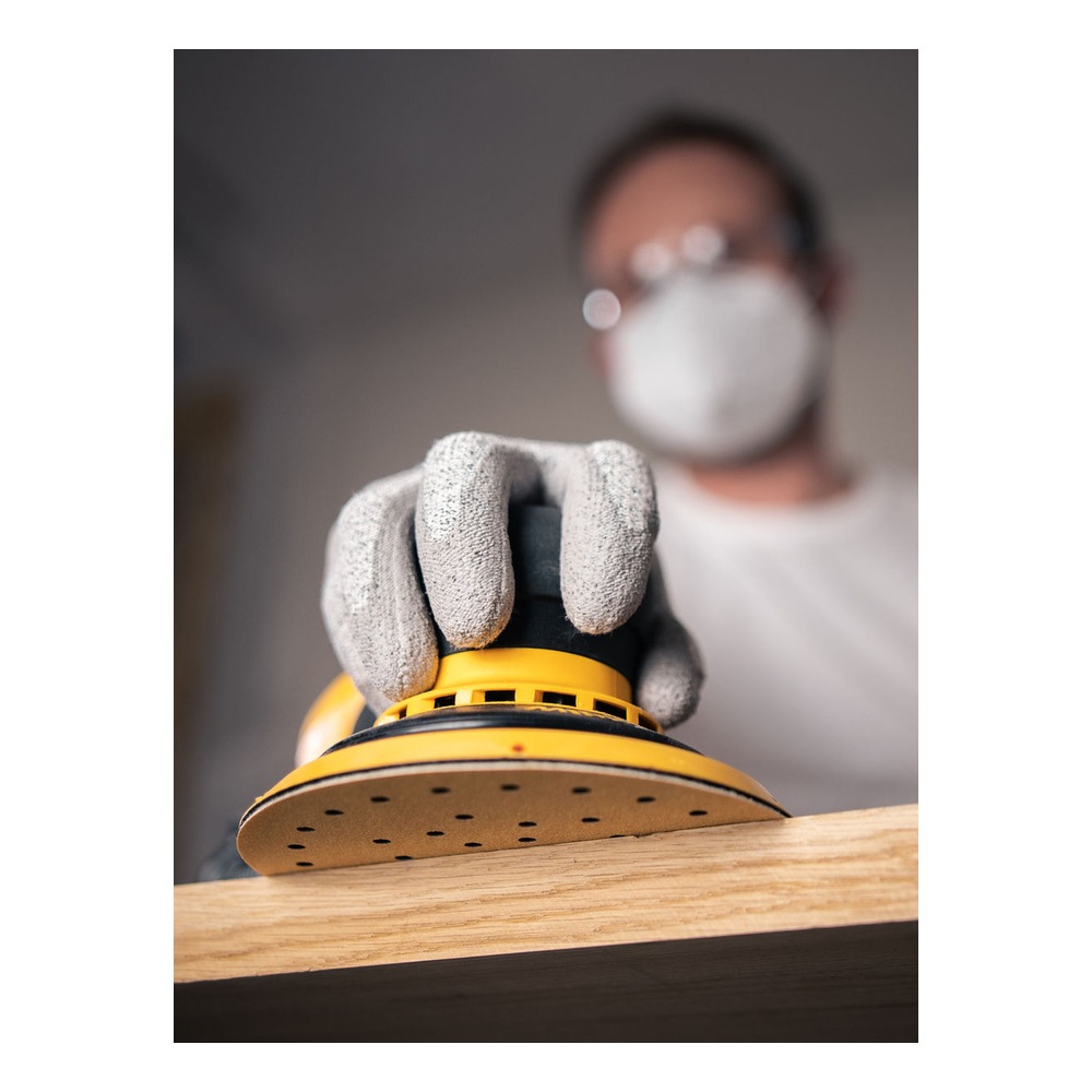 Close-up of a yellow and black round sander on the edge of a wooden board