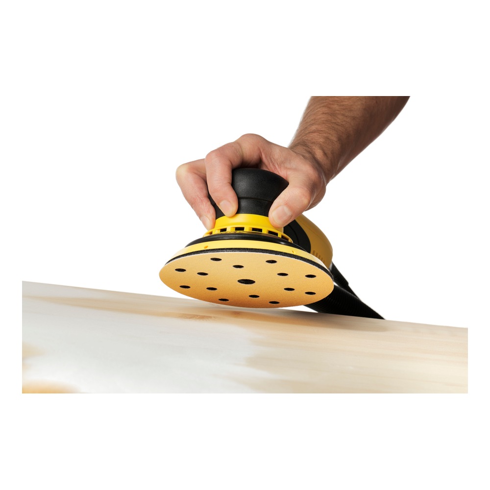A hand holding a round sander in use on a light wood surface, angled side