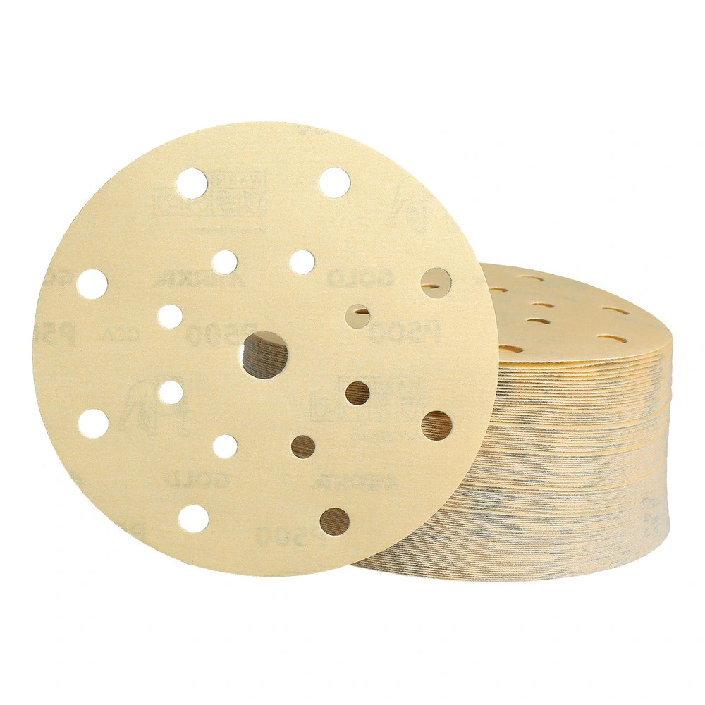A gold perforated round sanding disc with a stack of discs behind it, front