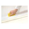 A hand holds a yellow sanding sheet against a white surface during sanding