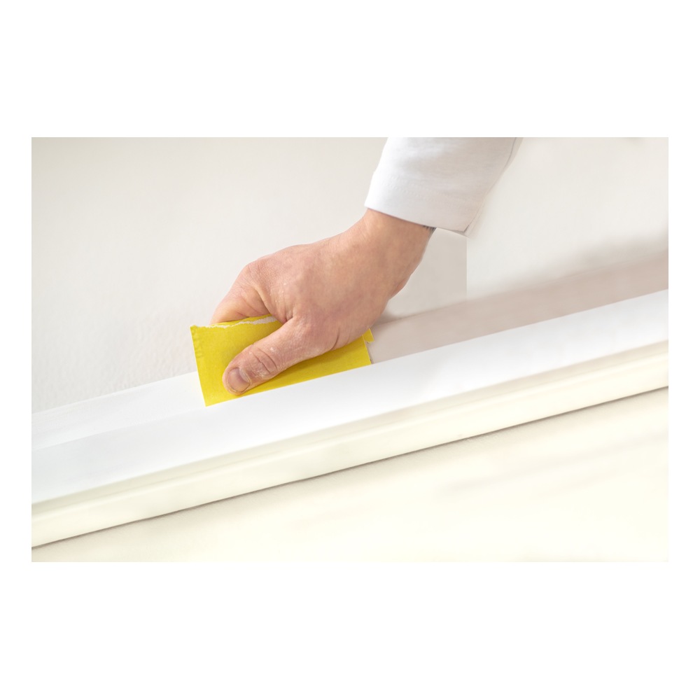 A hand holds a yellow sanding sheet against a white surface during sanding