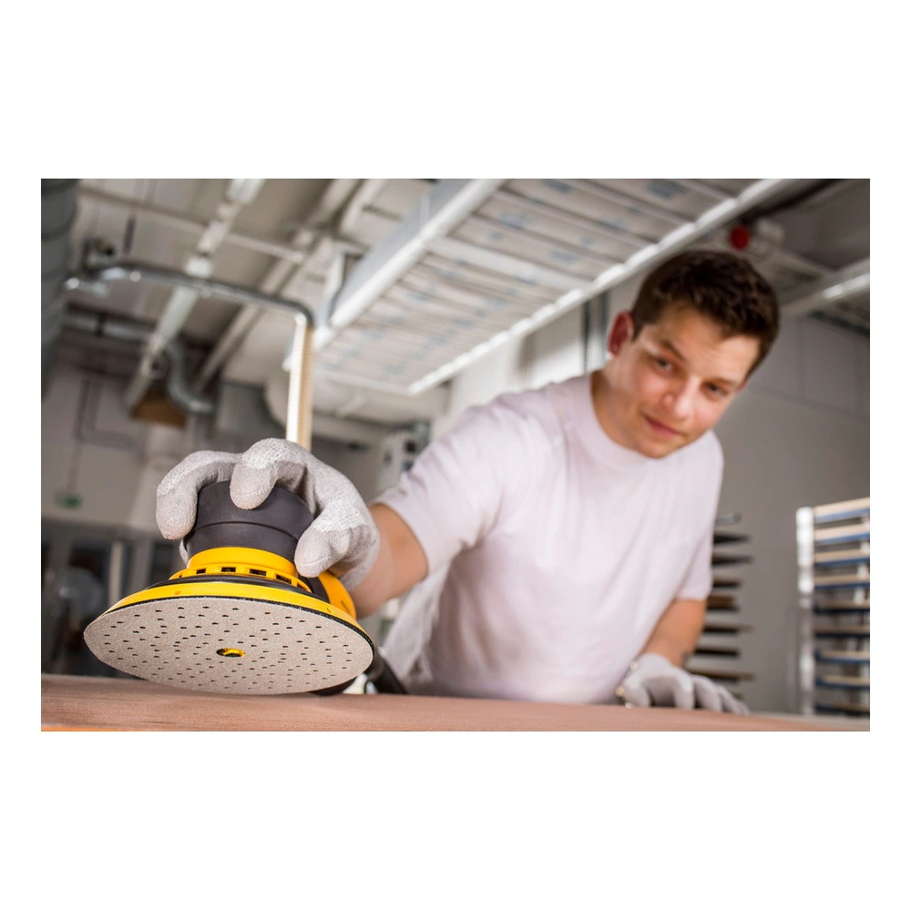 A person using a yellow-and-black round sander on a wood surface in a work