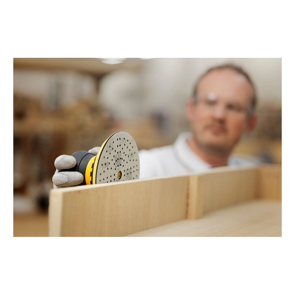 A person is holding a perforated sanding disc against a wooden surface