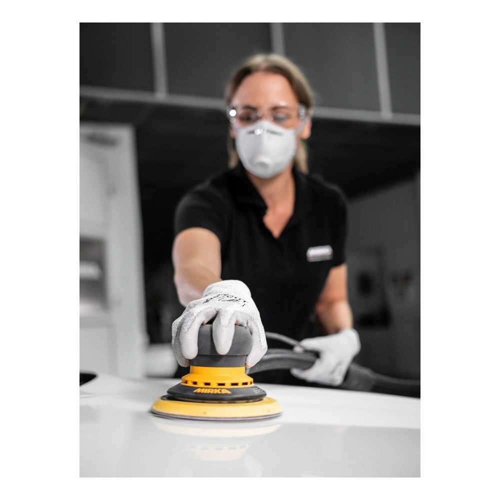 A person wearing a mask and safety glasses uses a yellow-and-black round