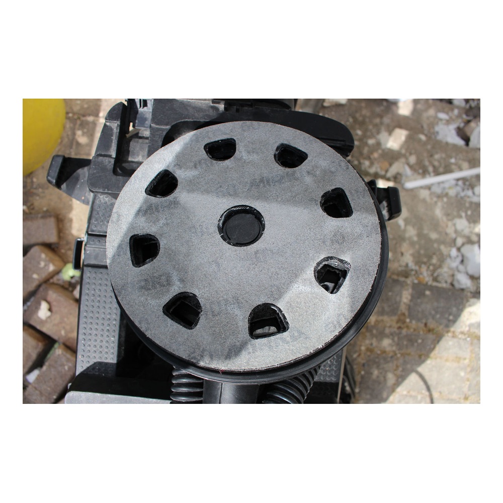 Close-up of a round perforated sanding disc mounted on a black power tool