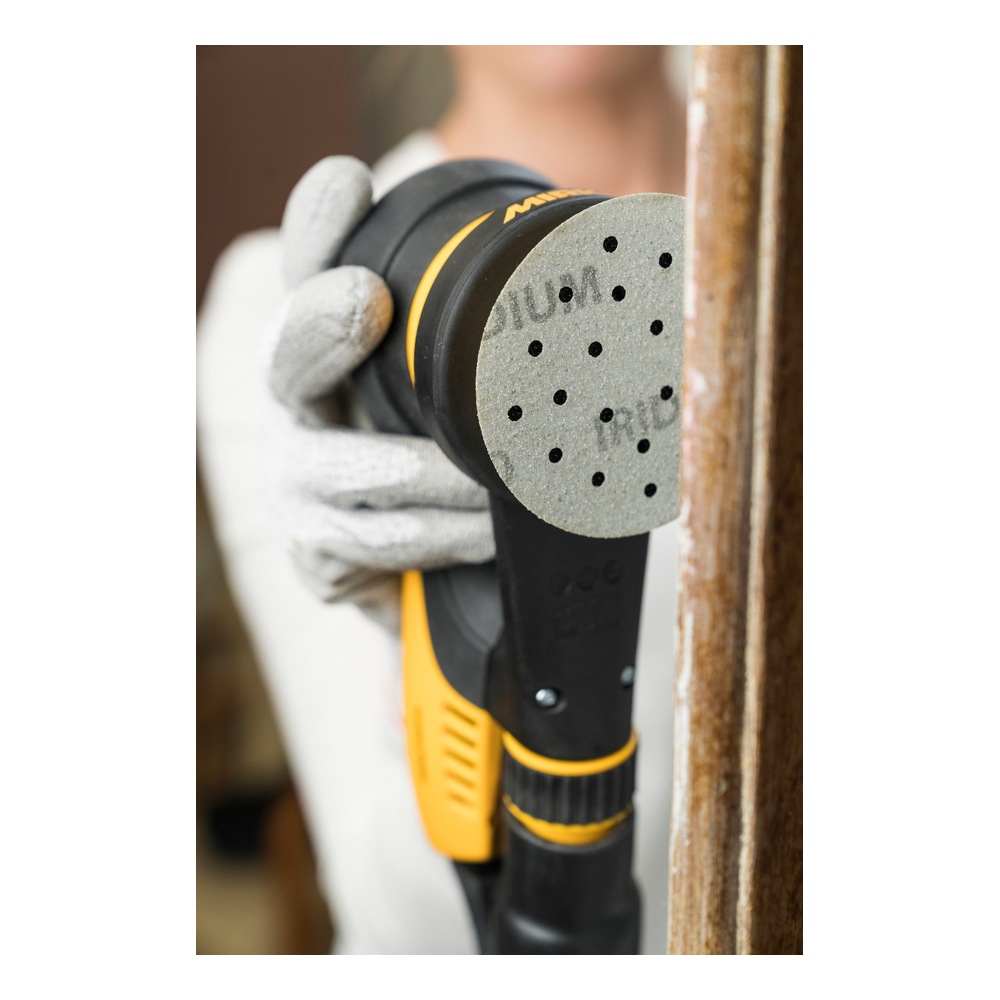 A person holds a black-and-yellow hand sander with a gray perforated sanding