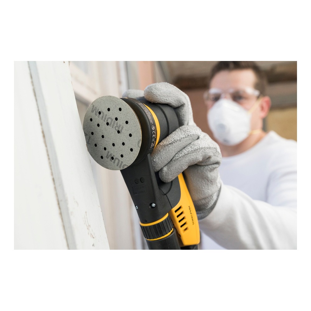 Person wearing safety glasses and a dust mask using a yellow and black round