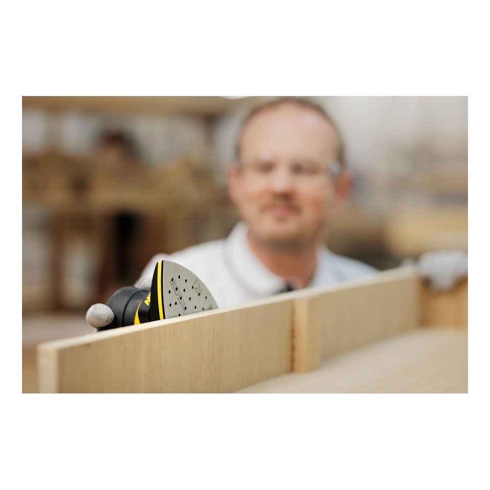 A blurred person in the background is holding a triangular sanding tool