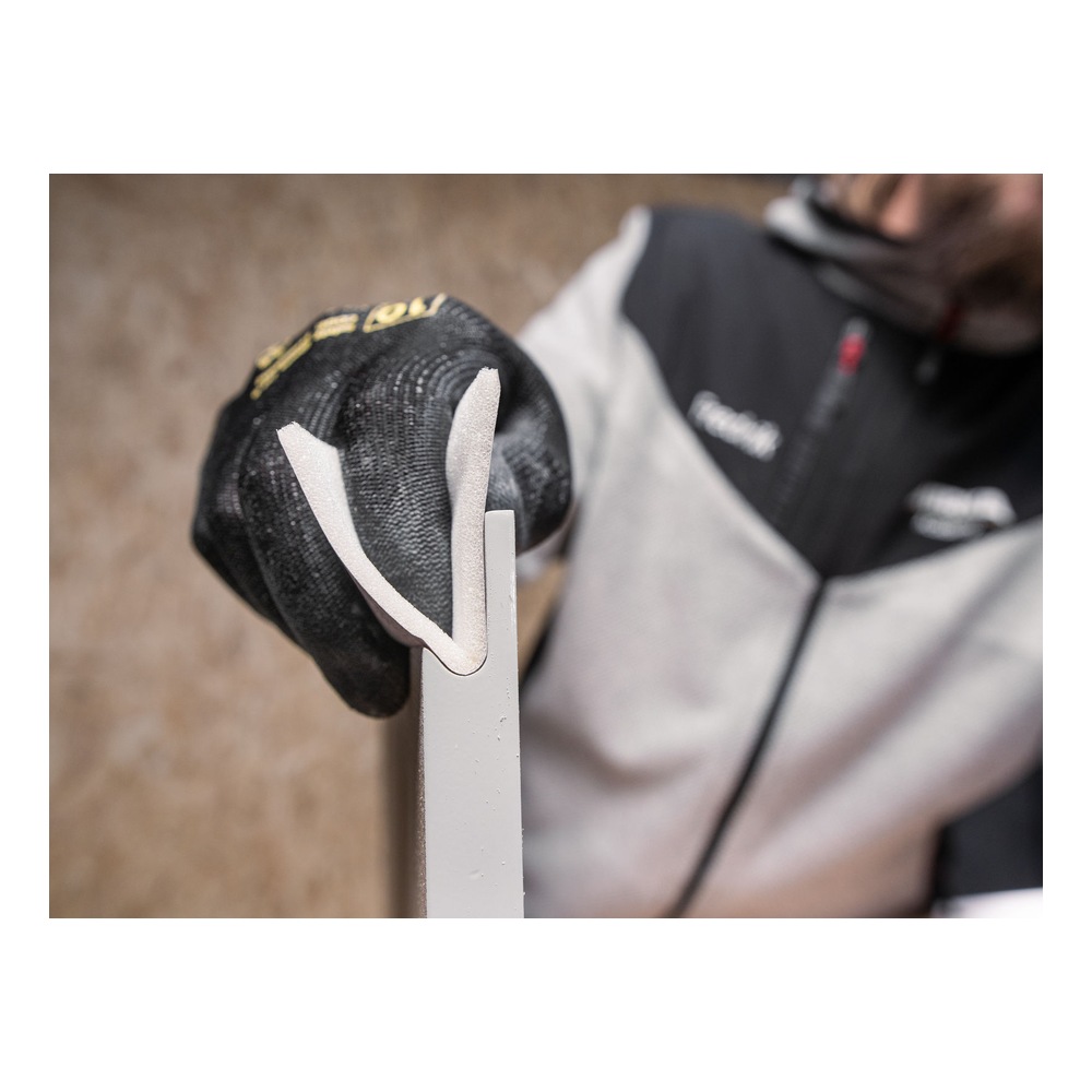A person wearing a glove is holding a folded sanding sheet around the edge