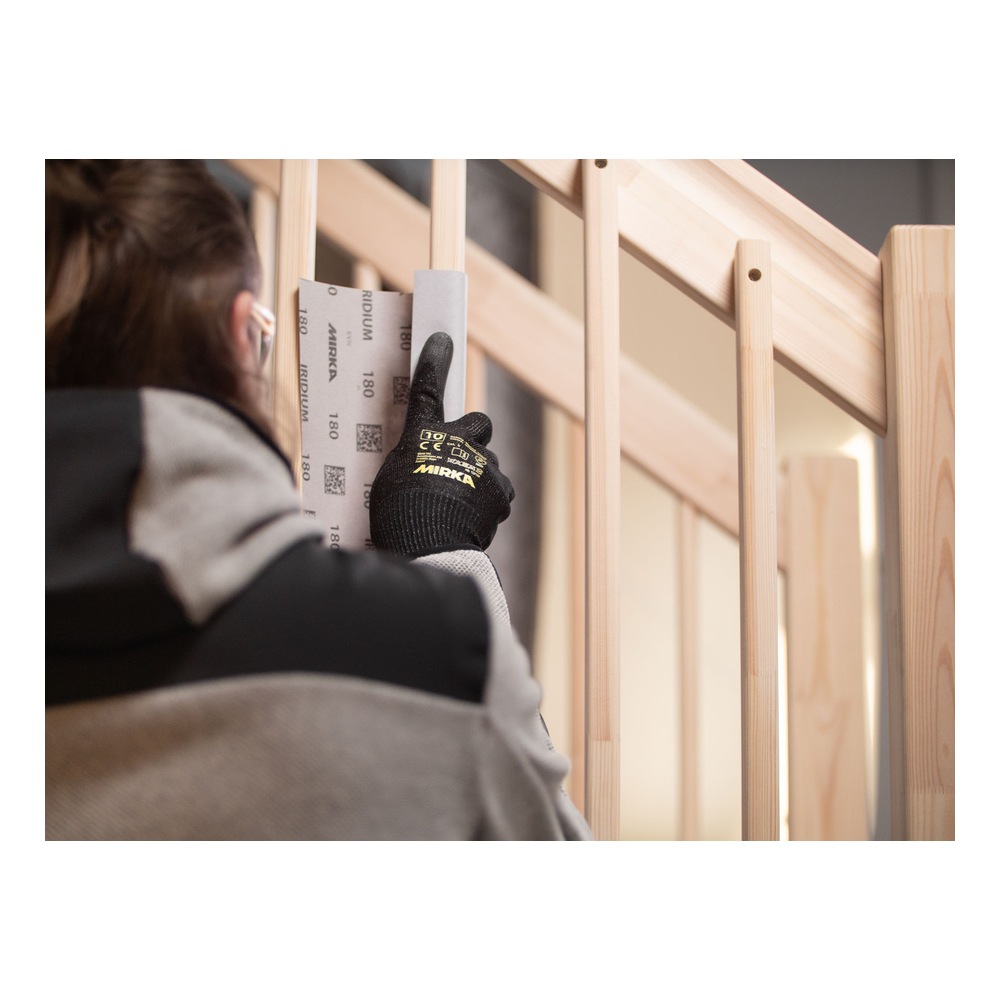 A gloved person holding a gray sanding sheet against wooden frame parts